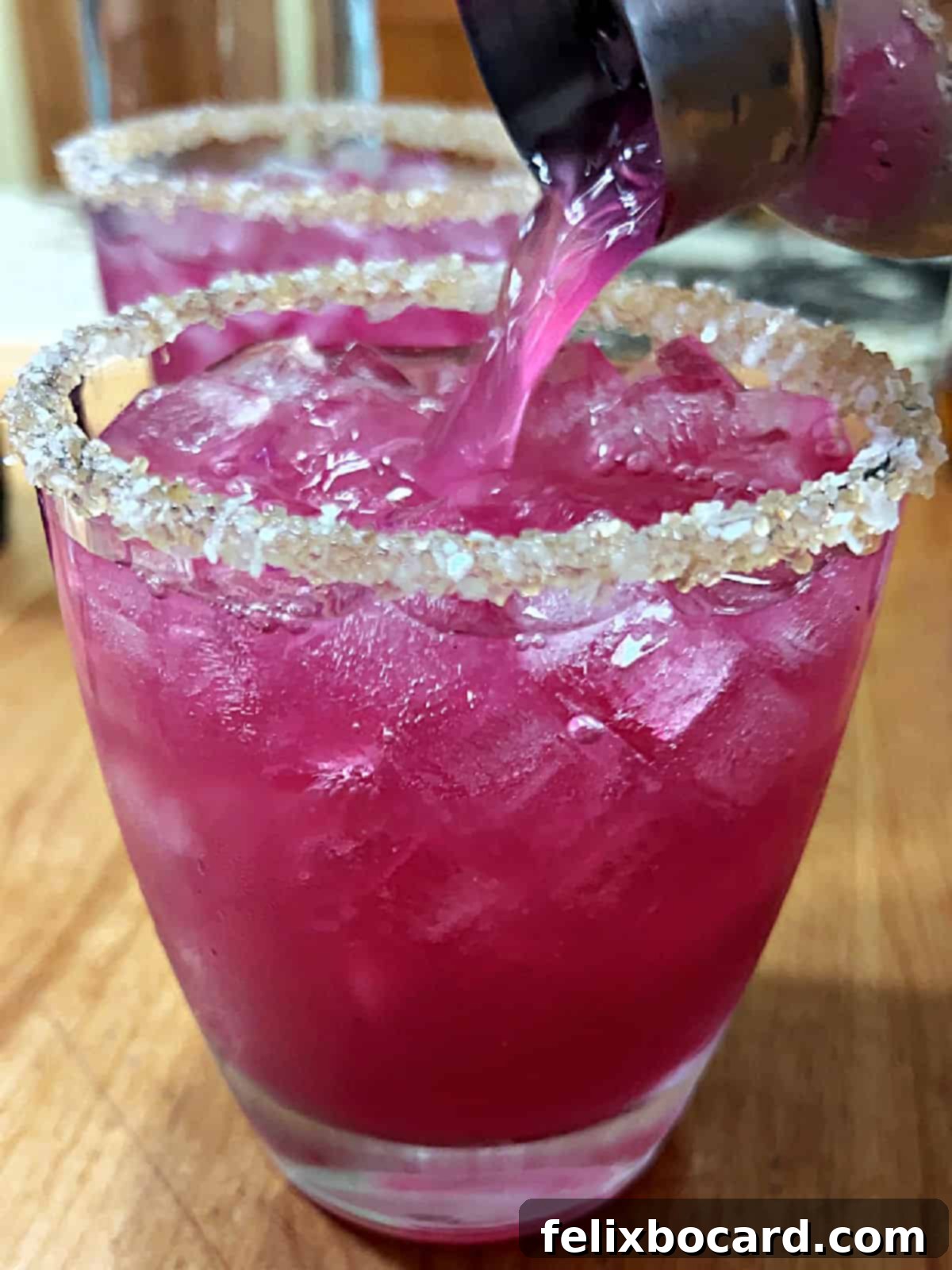 Pouring the vibrantly pink prickly pear margarita from a shaker into an ice-filled, garnished glass.