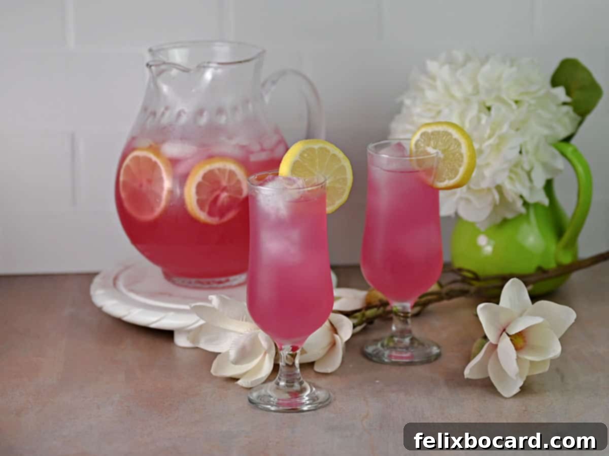 Desert Rose Lemonade 2 Two glasses of vibrant pink prickly pear lemonade, garnished with fresh lemon slices, with a pitcher of the drink in the background.