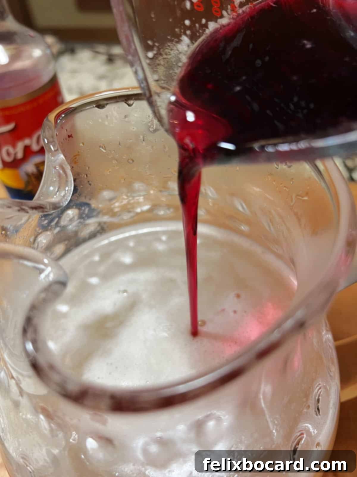 Desert Rose Lemonade 7 A hand pouring prickly pear syrup into a pitcher containing sweetened water and lemon juice.