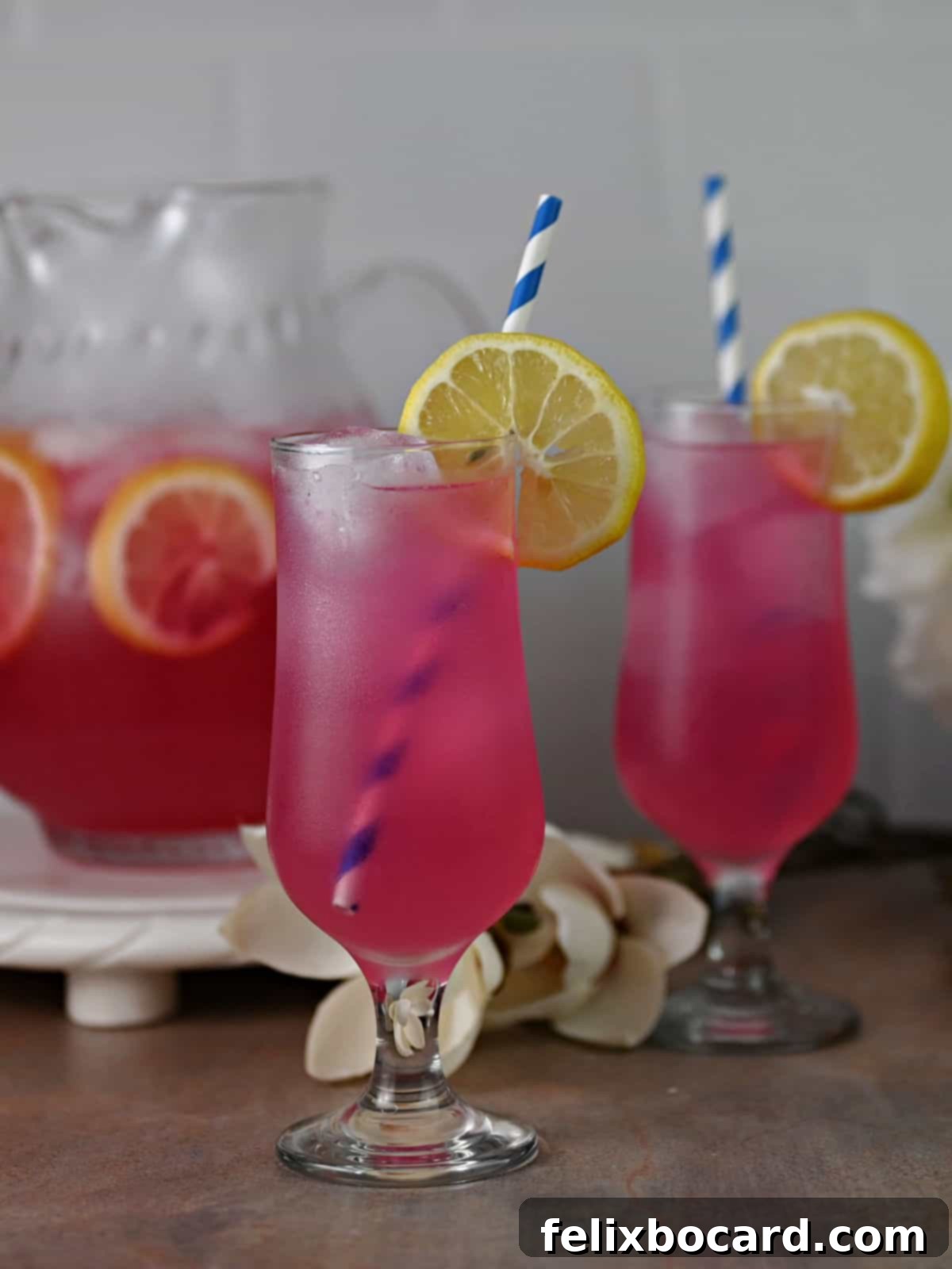 Desert Rose Lemonade 10 Two glasses of vibrant pink prickly pear lemonade, garnished with lemon slices and blue and white straws, ready for enjoyment.
