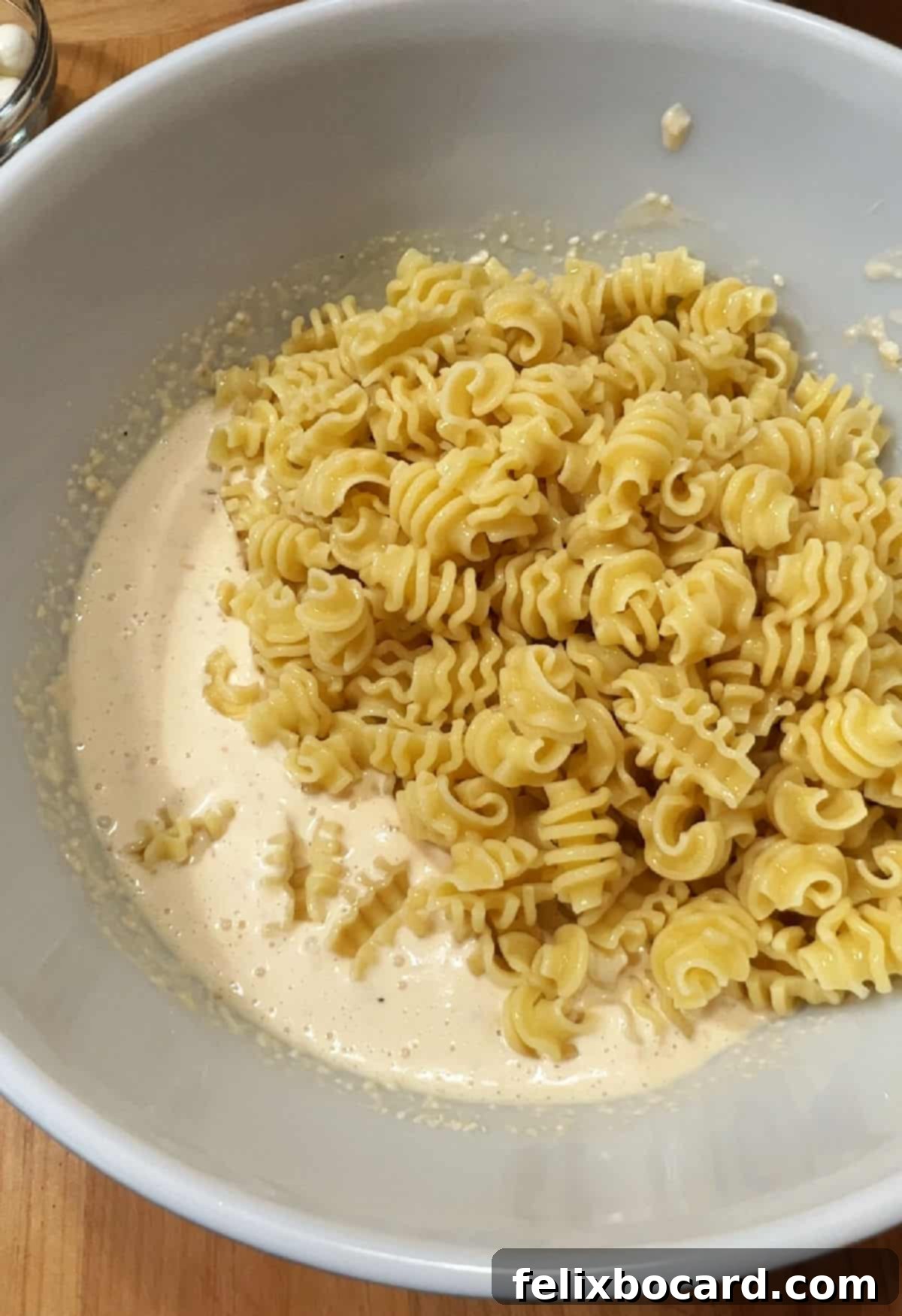 Adding cooked pasta to the bowl with dressing.