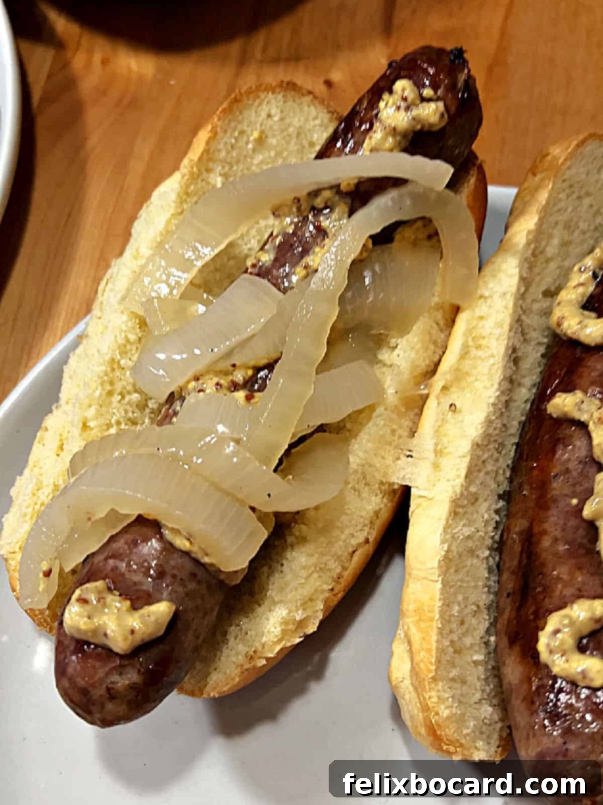 Classic Wisconsin Beer Brats 8 A delicious bratwurst in a bun, topped with stone ground mustard and savory beer-soaked onions, close-up.