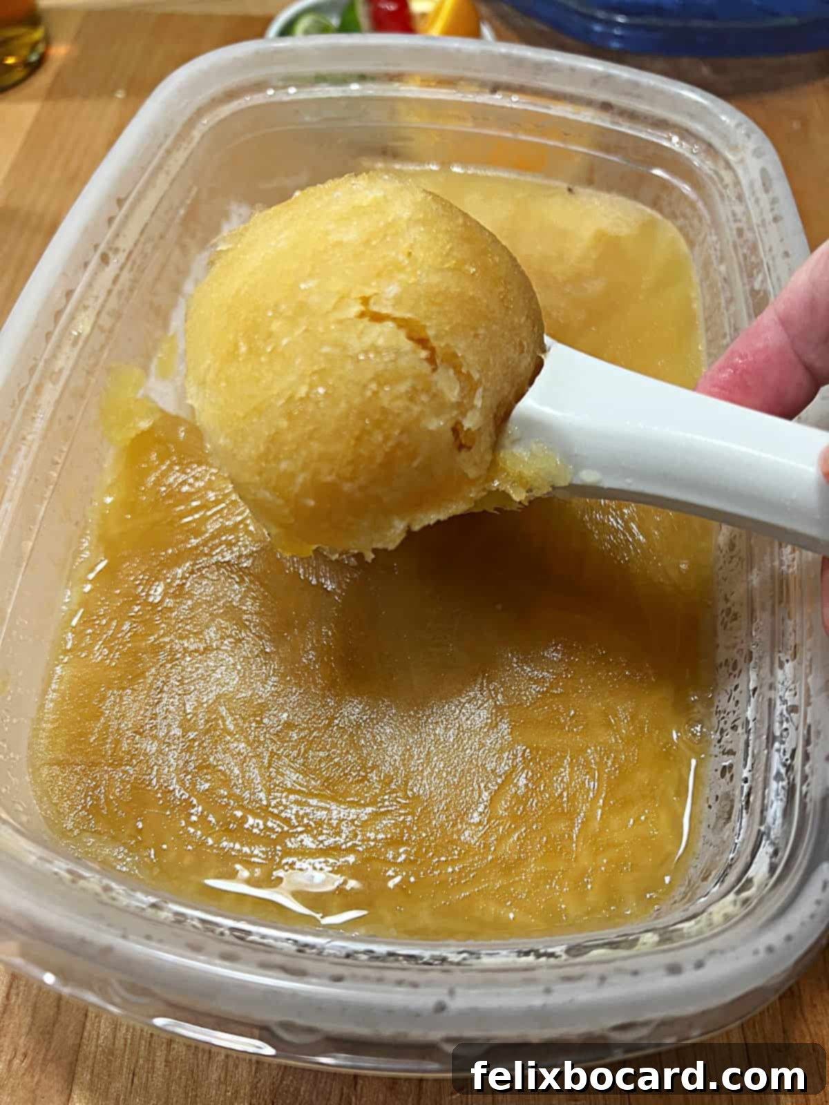 An ice cream scoop holds a generous portion of the shimmering, amber-colored frozen brandy slush, ready to be served.