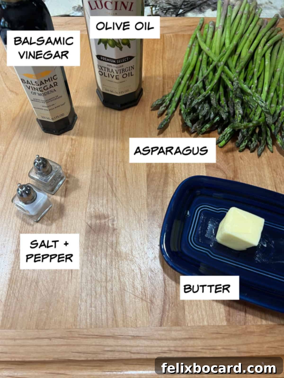 All ingredients laid out: fresh green asparagus, a bottle of olive oil, balsamic vinegar, a stick of butter, and salt and pepper shakers.
