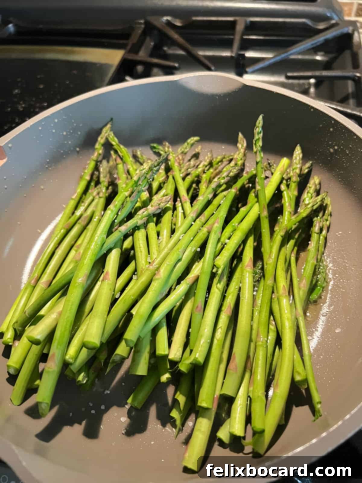 Fresh asparagus spears being sautéed in a hot skillet with olive oil.