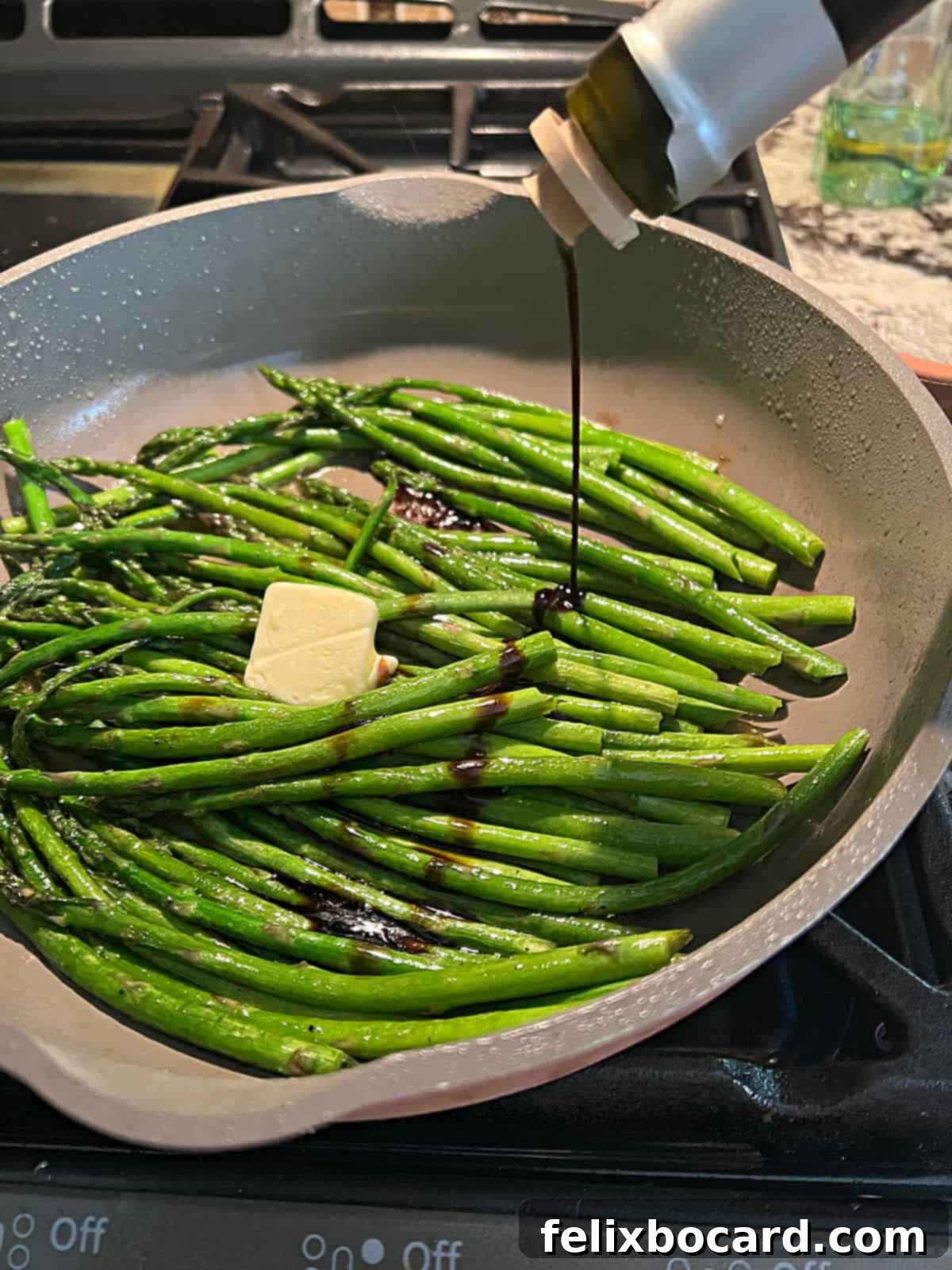 Balsamic vinegar being drizzled over sautéing asparagus in a pan.