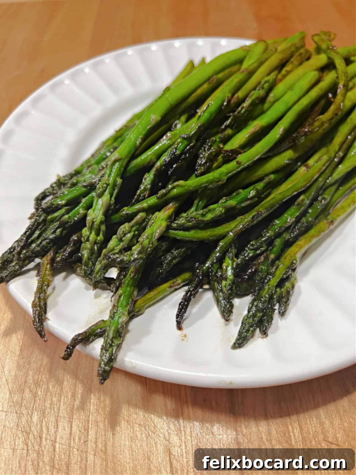 A serving plate filled with glossy, sautéed asparagus spears coated in balsamic vinegar.