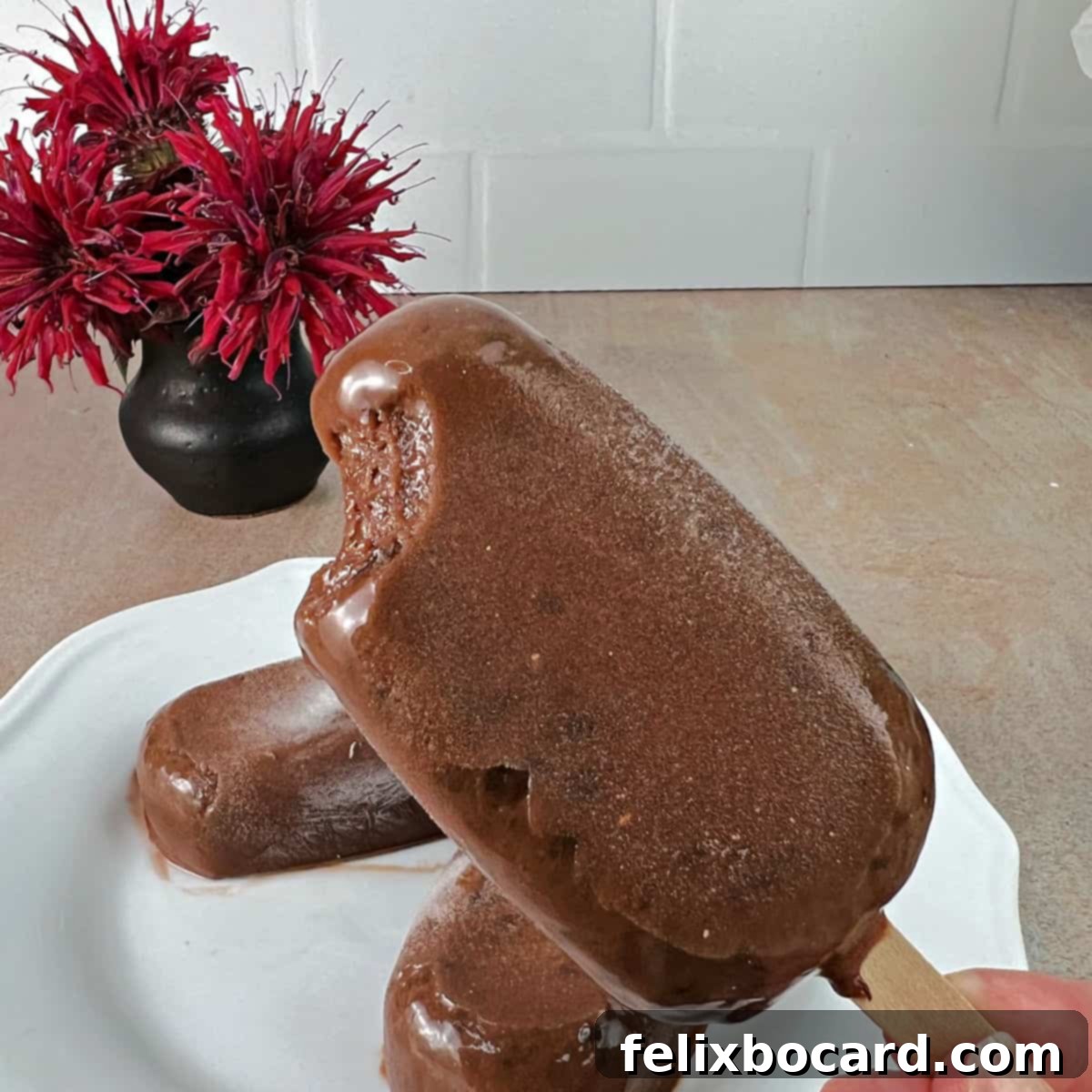 A homemade fudgesicle with a significant bite taken out, showing the deep chocolate color and creamy interior, ready to be enjoyed. A close-up view.