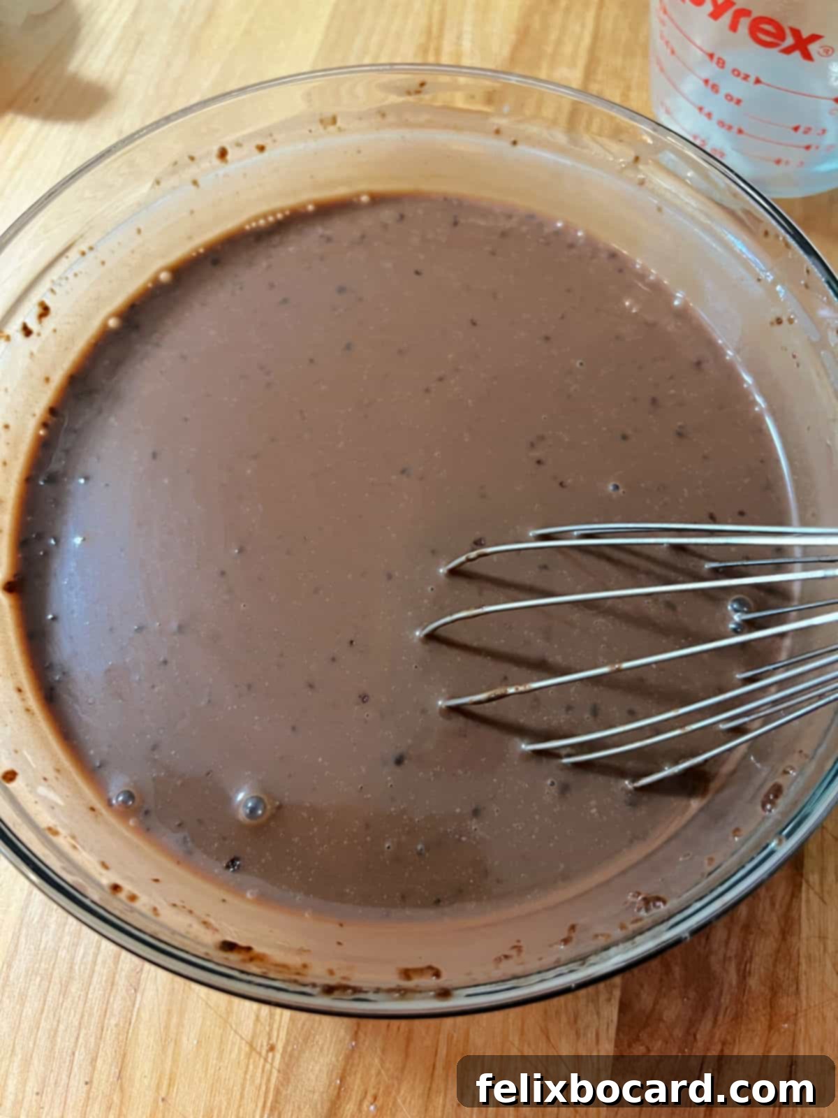 A close-up shot of dry chocolate instant pudding mix being whisked into a bowl of milk, creating a smooth chocolate liquid. The whisk is in motion.