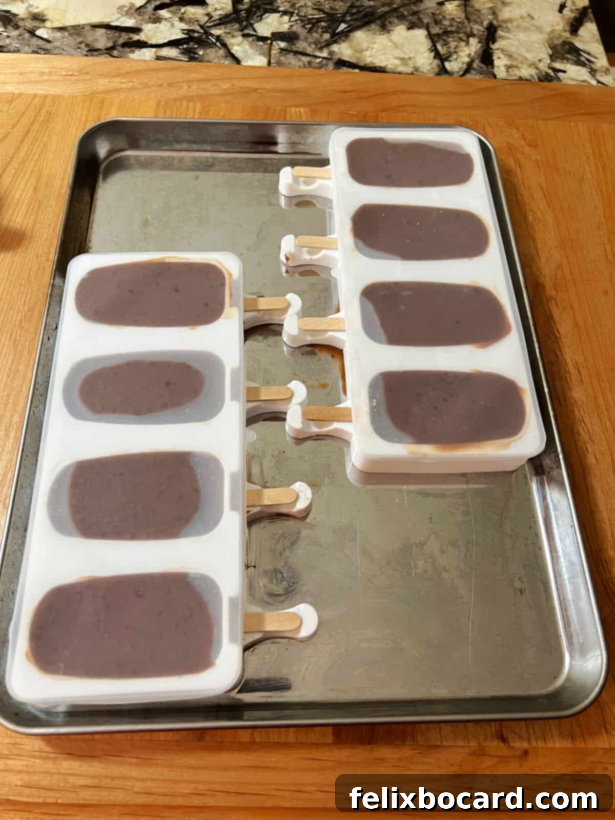 Popsicle molds filled with the fudgesicle mix and wooden sticks inserted, neatly arranged on a tray and ready to freeze.