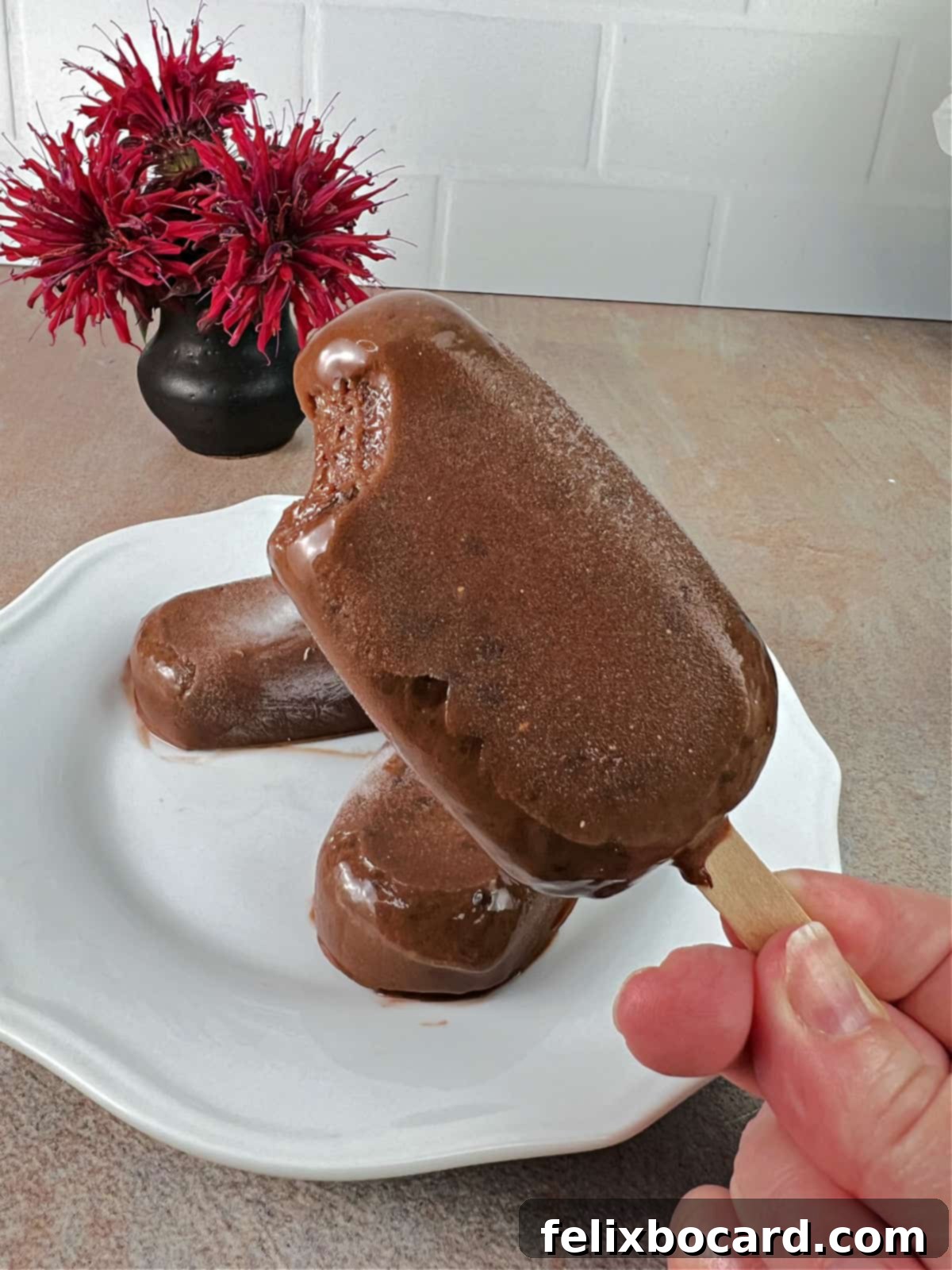 A homemade fudgesicle with a significant bite taken out, showing its smooth, creamy, dark chocolate interior against a light background. A truly tempting treat.