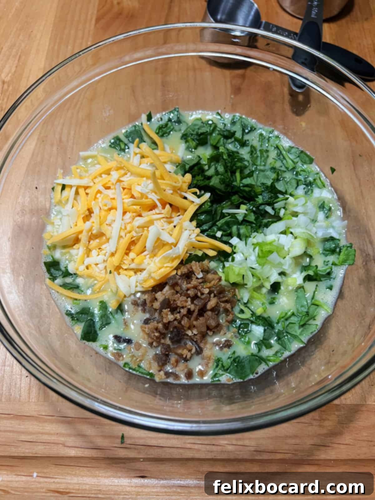 Egg mixture ready for stirring, topped with spinach, bacon bits, green onion, and cheese.