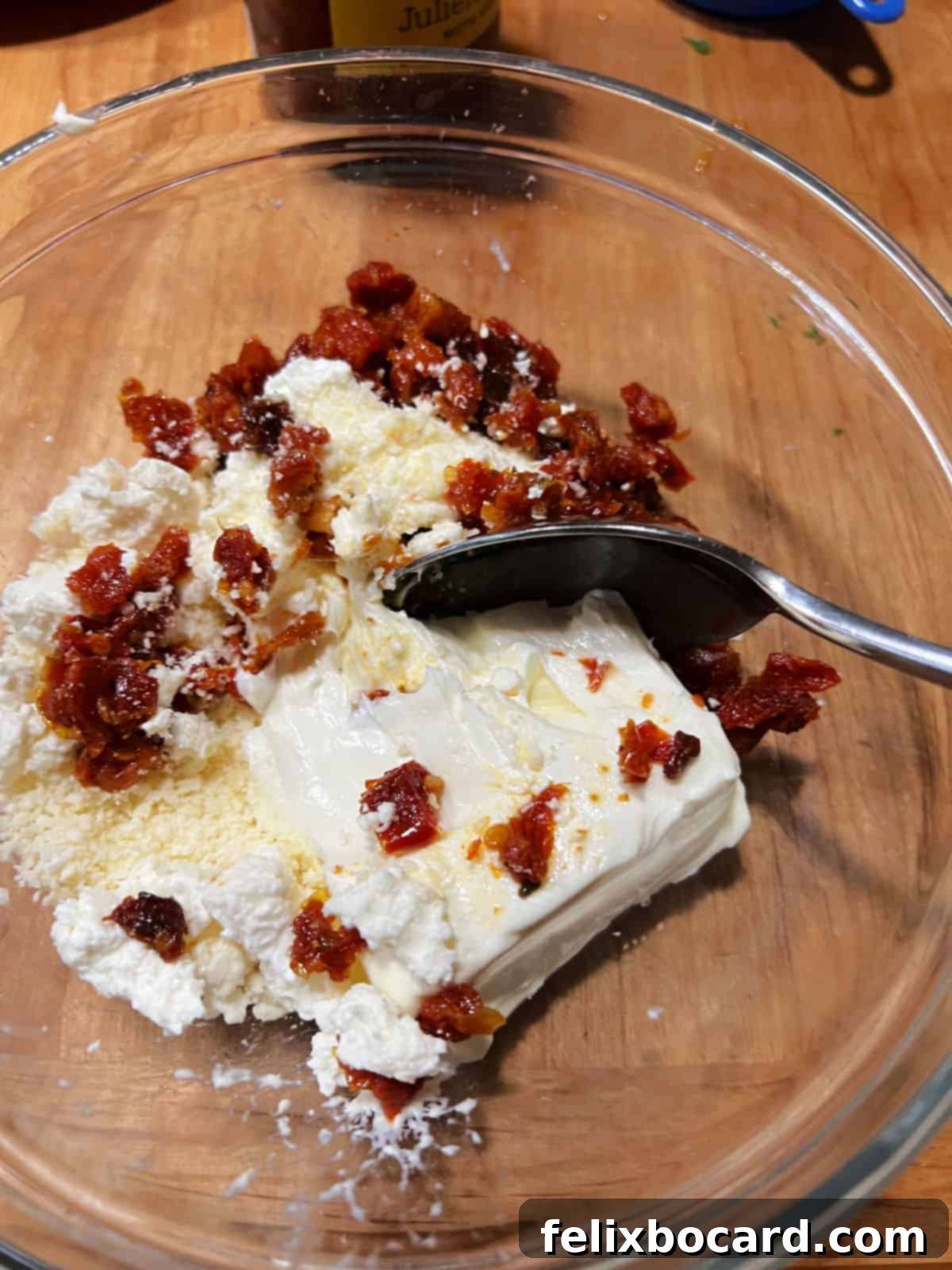 Mixing cream cheese with sun dried tomatoes and cheeses.