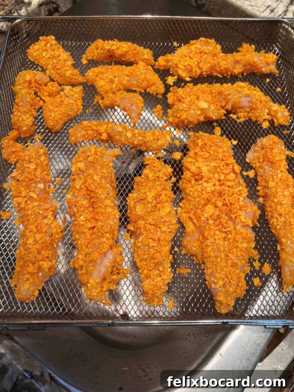 Crunchy Doritos Air Fryer Chicken Tenders 9 Neatly arranged Doritos coated chicken tenders in an air fryer basket, ready for cooking.