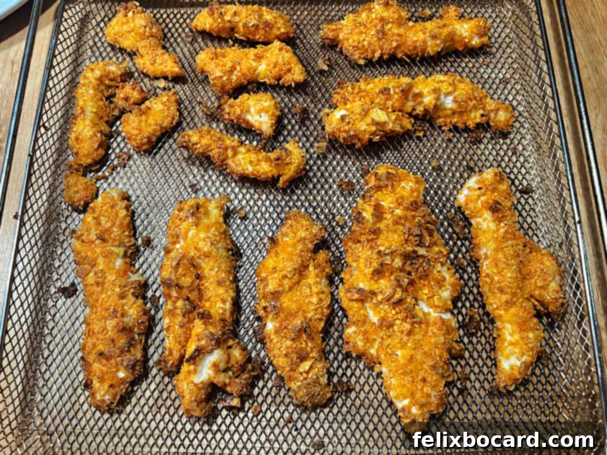 Crunchy Doritos Air Fryer Chicken Tenders 10 Air fryer cooked Doritos chicken tenders being removed from the basket onto a plate.