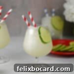 Blended Daiquiri Bliss 10 Frozen Daiquiri slush in a stemmed cocktail glass, garnished with a lime wheel, with striped straws for drinking.