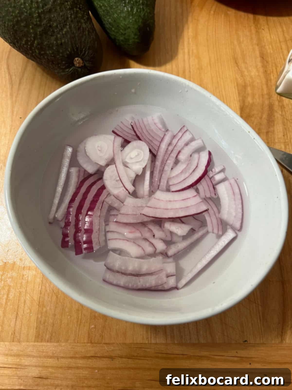 Thinly sliced red onion soaking in a bowl of water, a technique to reduce its sharpness.