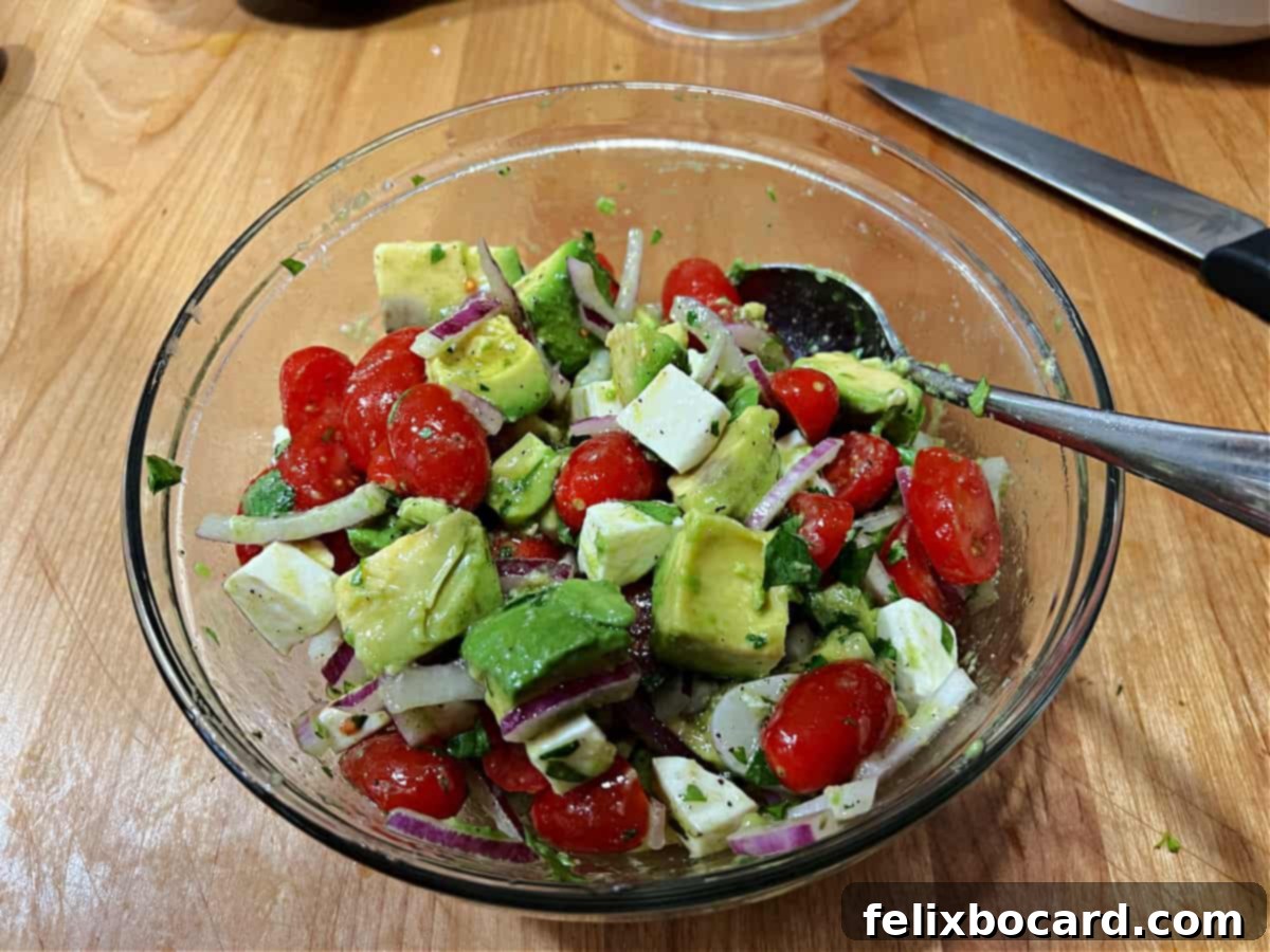 All ingredients for Mexican Avocado Salad tossed together and coated with dressing, presented in a mixing bowl.