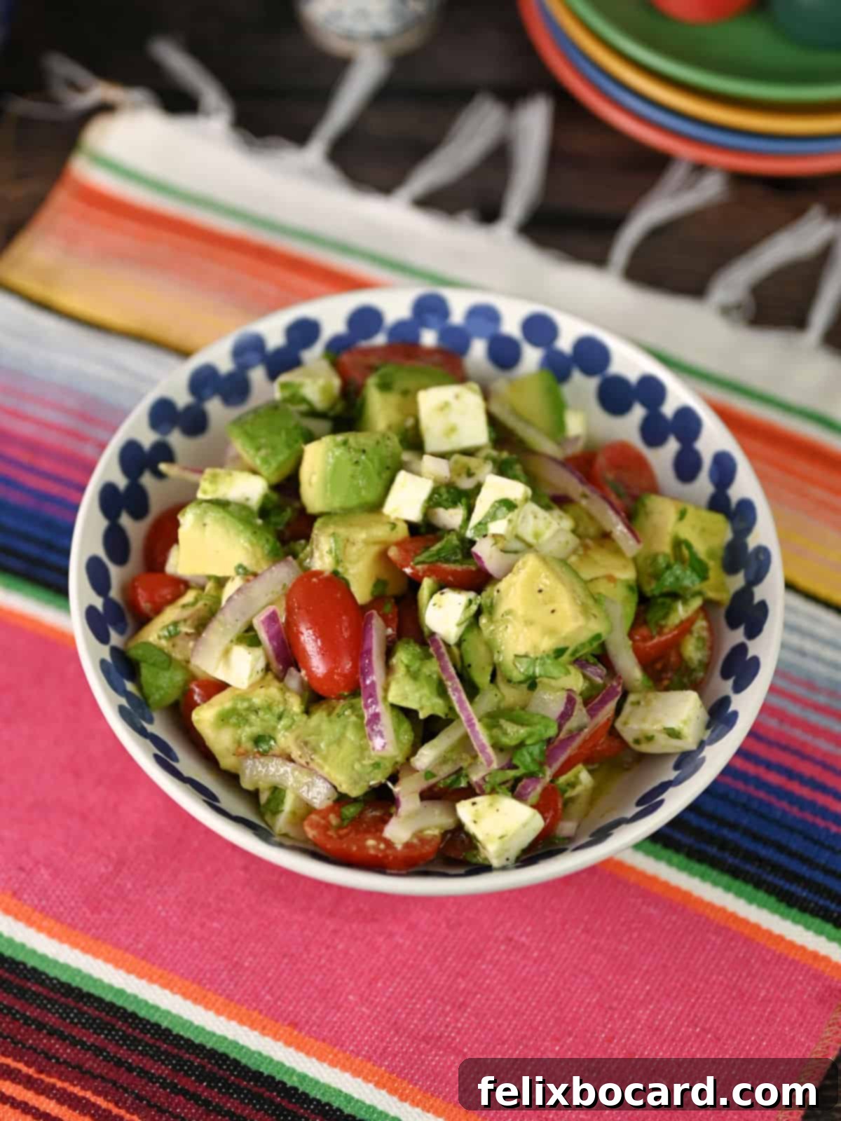 A bowl of fresh Mexican Avocado Salad placed on a colorful, striped Mexican blanket, highlighting its vibrant appeal.