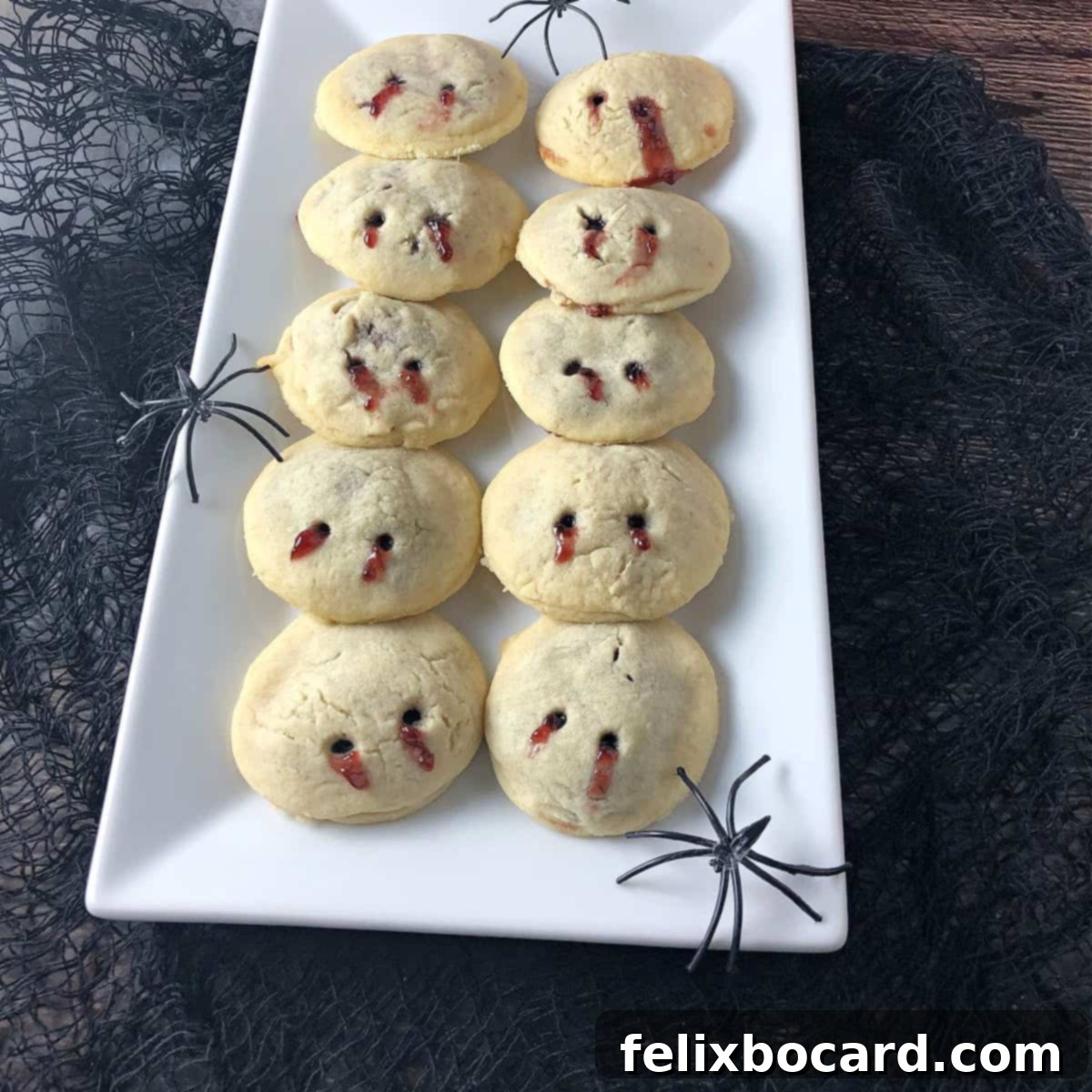 Monster Mash Punch 11 Vampire kiss cookies on a rectangular white plate, a couple spiders lurking around