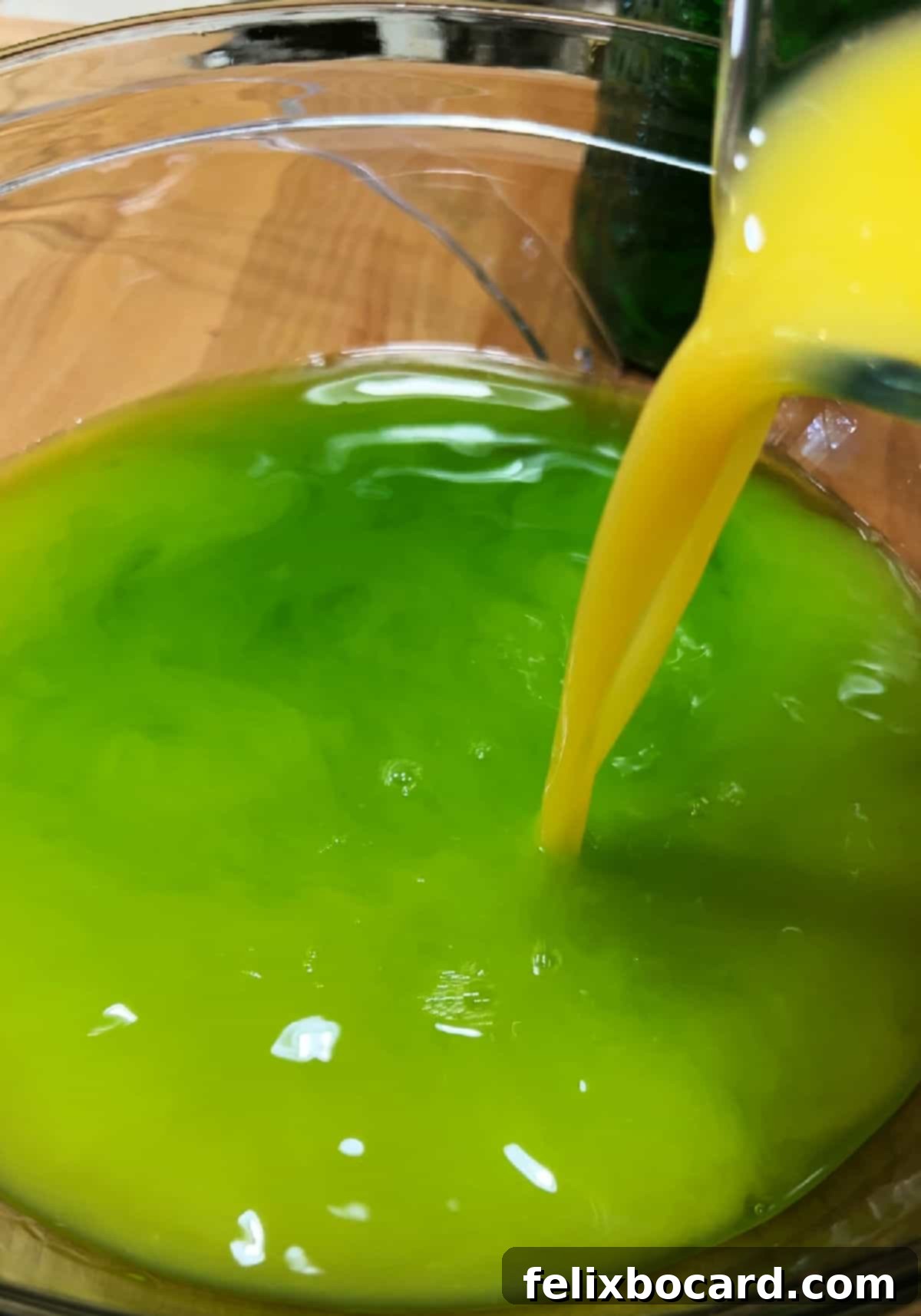 Monster Mash Punch 5 Adding orange juice to the green liqueur in the bowl.