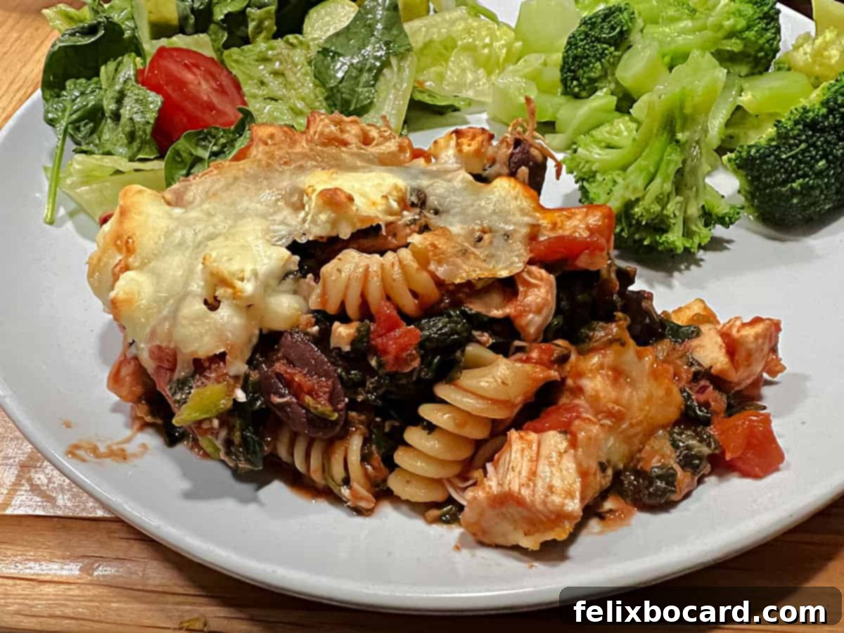 Greek chicken and pasta casserole served on a plate with salad and vegetable.