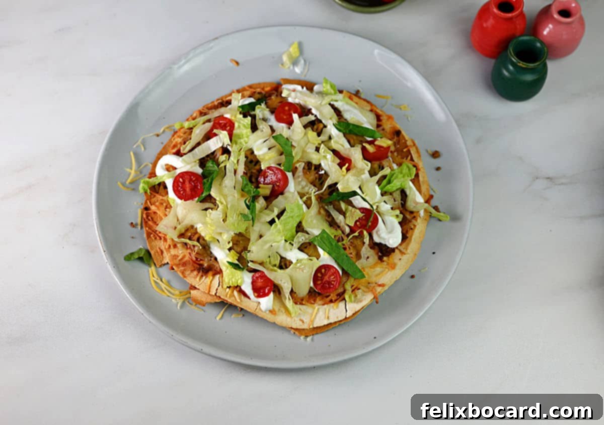 Finished Mexican pizza topped with lettuce, tomato, and sour cream.