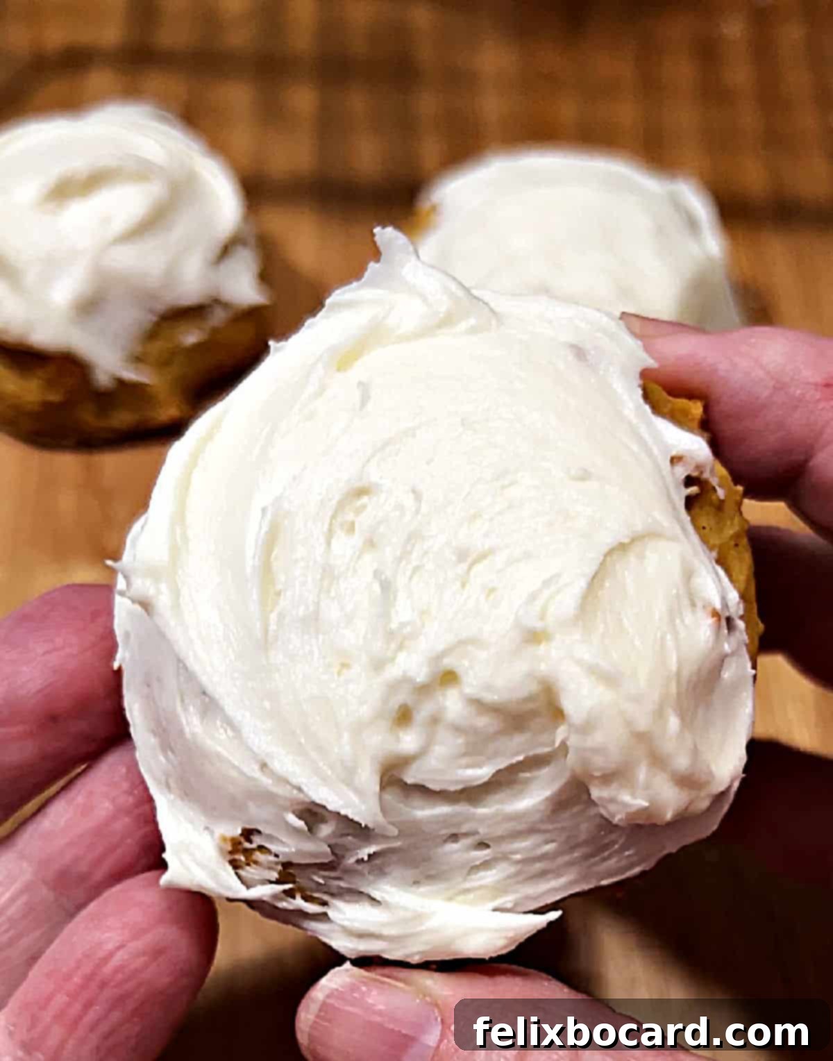Hands holding a pumpkin cookie with cream cheese frosting.
