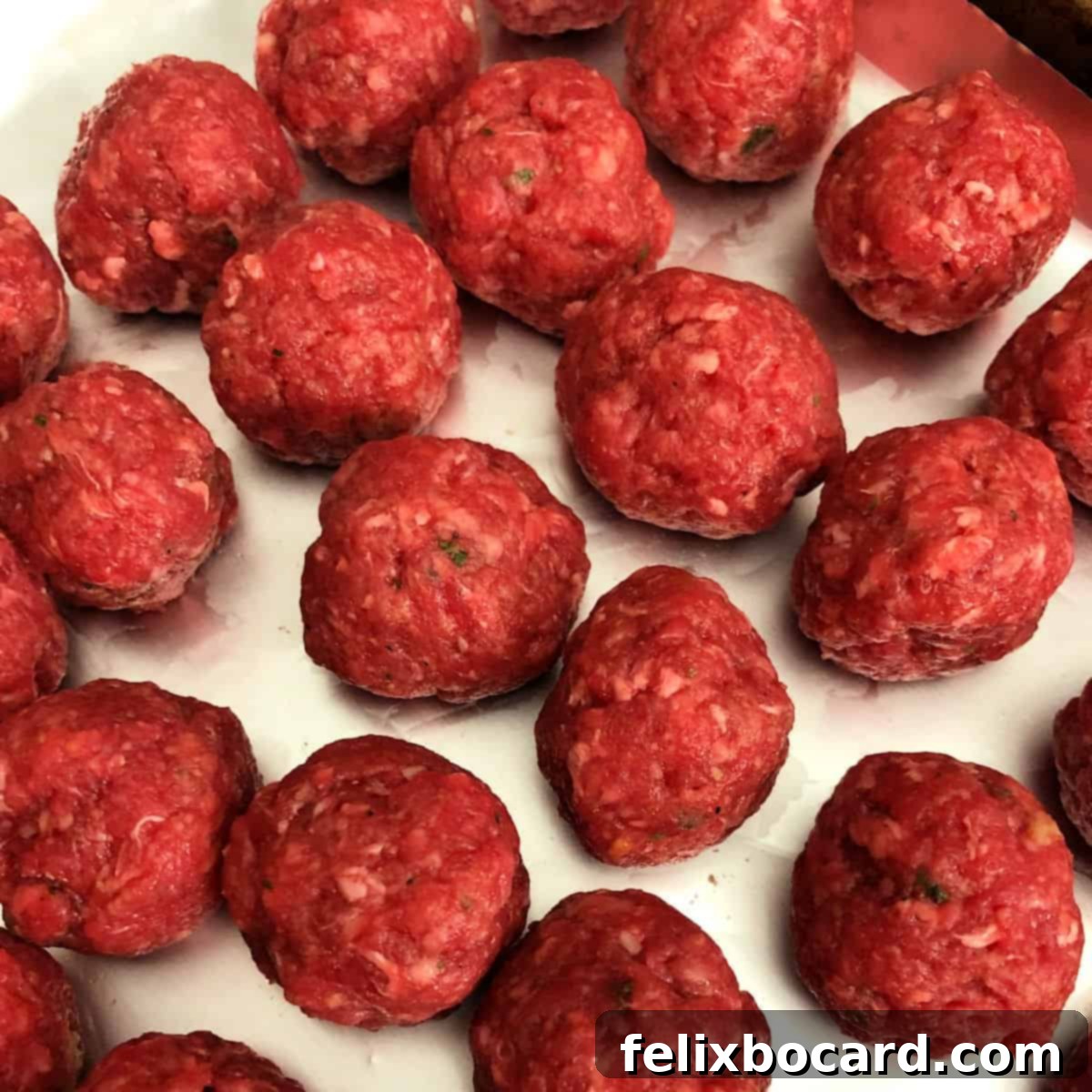 Make Ahead Freezer Meatballs 4 Rows of uncooked, perfectly formed meatballs neatly arranged on a parchment-lined baking sheet, spaced out and ready for the oven to become delicious freezer meatballs.