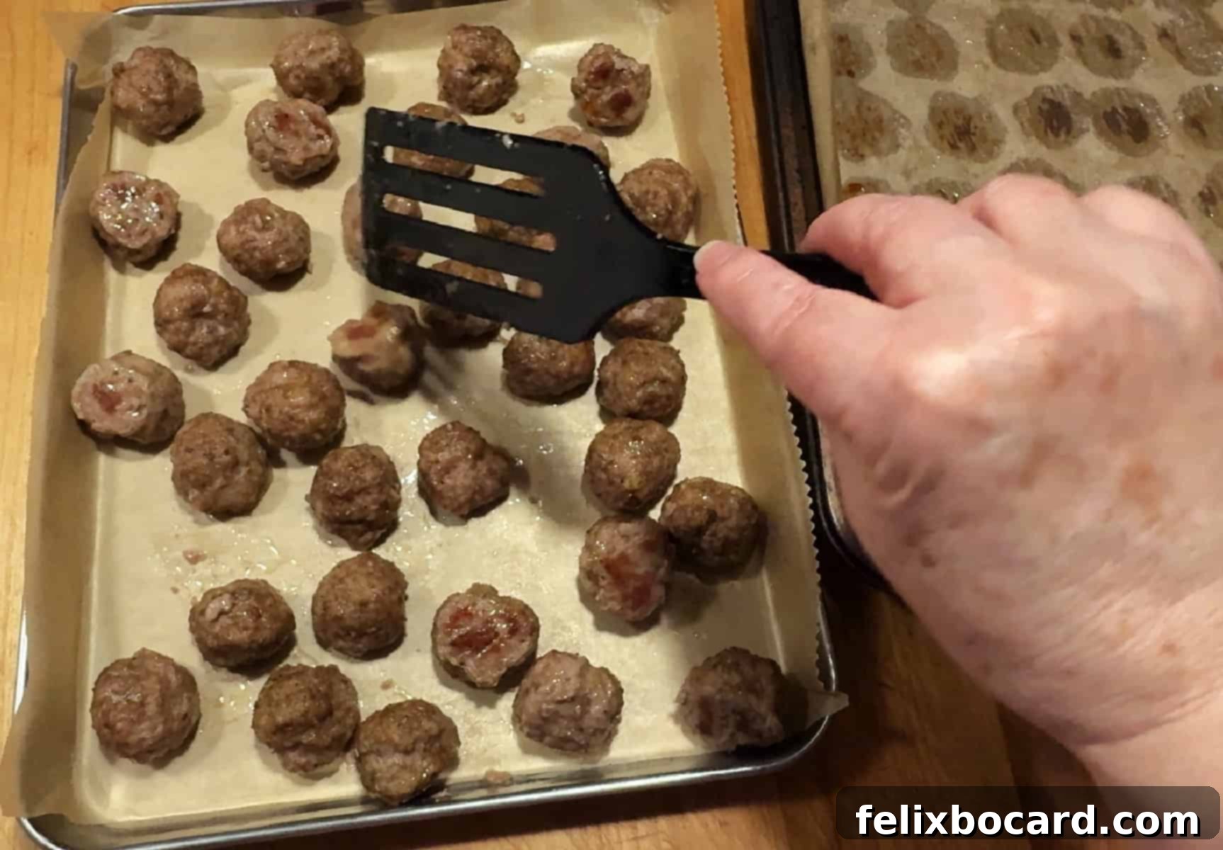 Make Ahead Freezer Meatballs 6 A hand gently transfers golden-brown cooked meatballs from one baking sheet to another fresh, parchment-lined tray for flash freezing, ensuring they don't stick together.