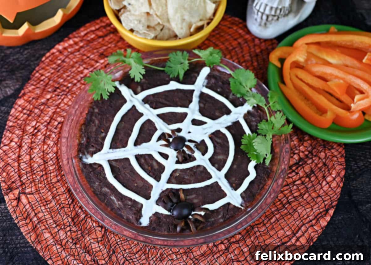 A mesmerizing sour cream spider web intricately spread over a rich black bean dip, served alongside crisp tortilla chips and vibrant bell pepper slices, perfect for a Halloween party.
