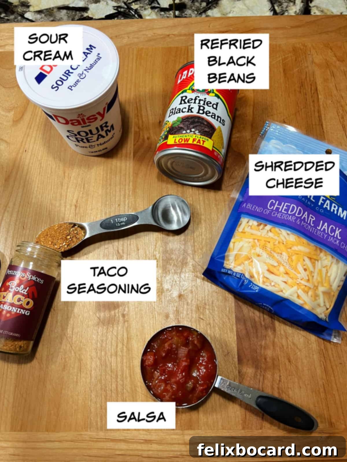 Key ingredients for the Spider Web Black Bean Dip laid out: sour cream for the web, refried black beans, shredded cheese, taco seasoning, and vibrant salsa.
