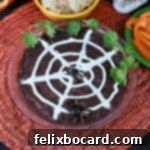 A festive close-up of the Spider Web Black Bean Dip, topped with a sour cream web and a black olive spider, ready for a Halloween celebration.