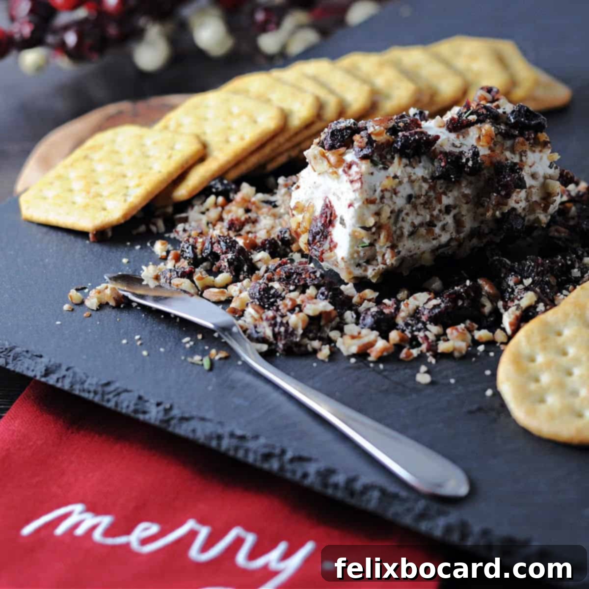 More Than Twenty Dried Cranberry Creations 4 A festive cranberry goat cheese log displayed on a wooden cheese board, surrounded by an assortment of crackers and garnishes.