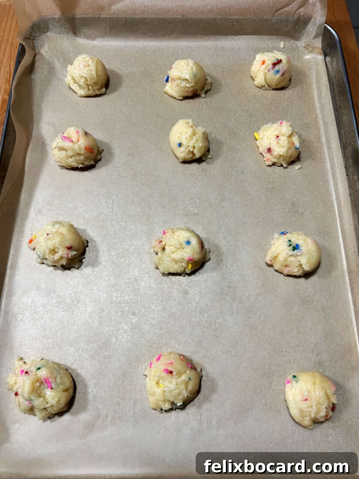 Balls of Funfetti cookie dough perfectly spaced on a parchment-lined baking sheet.