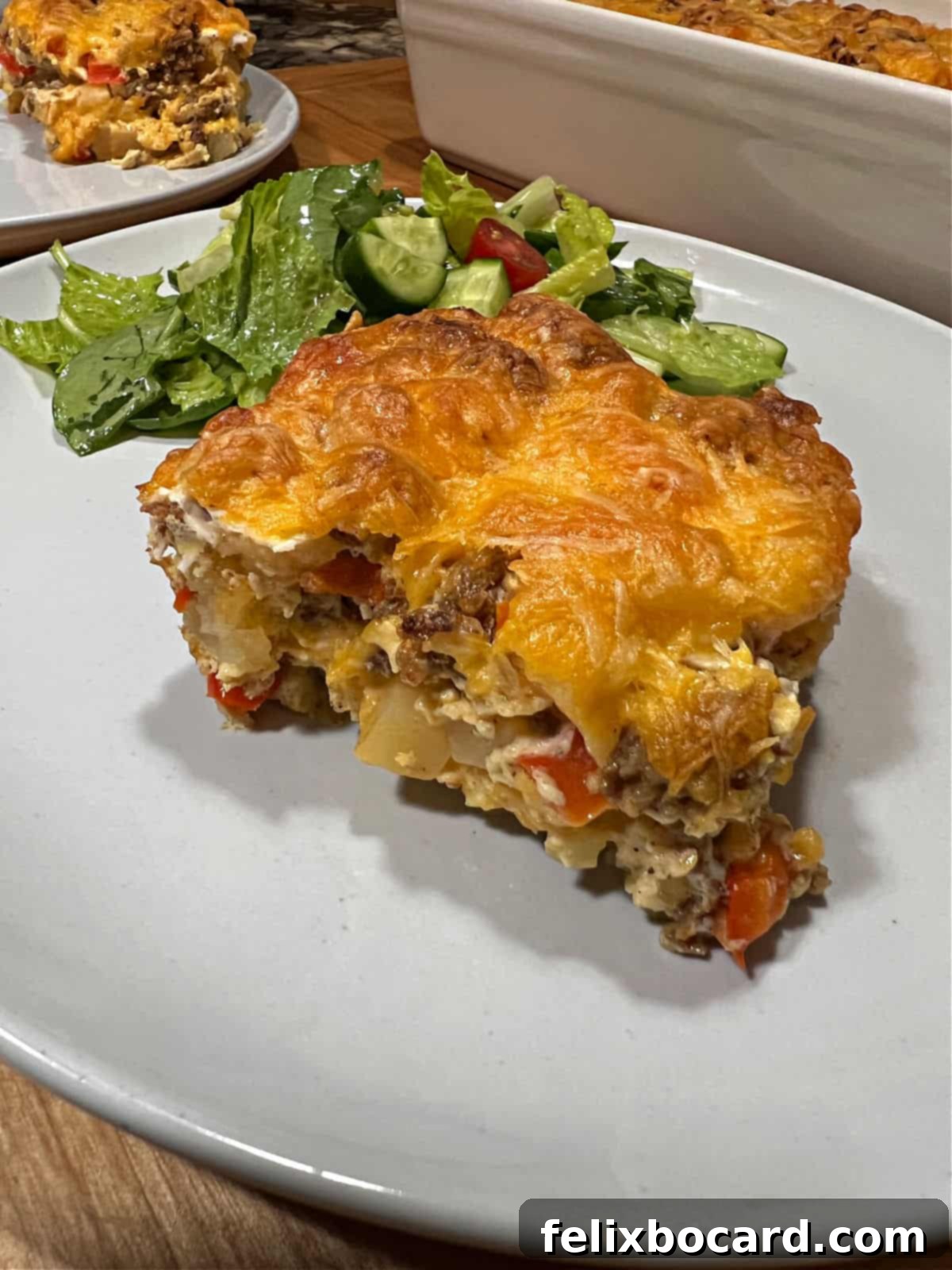 A square serving of Chorizo Egg Bake on a plate, garnished with fresh herbs and served alongside a light green salad.