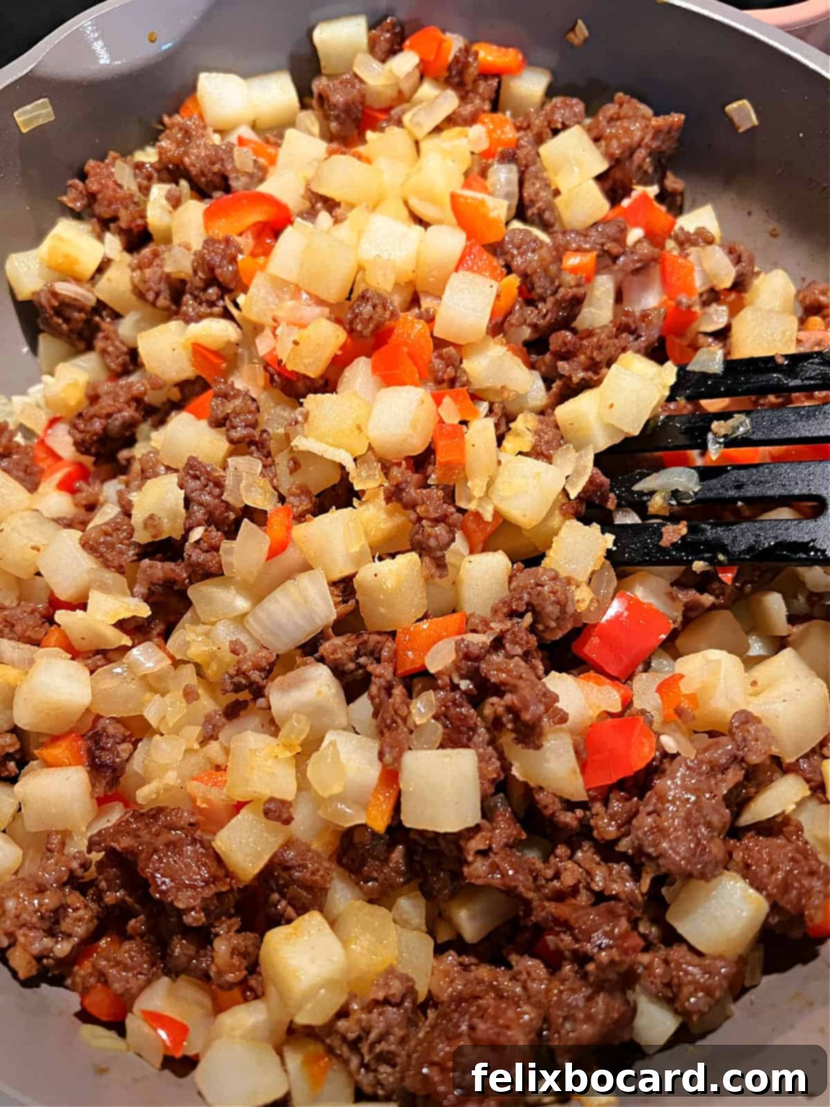 Cooked chorizo sausage being added back into the skillet with sautéed red bell peppers, onions, and hash browns.