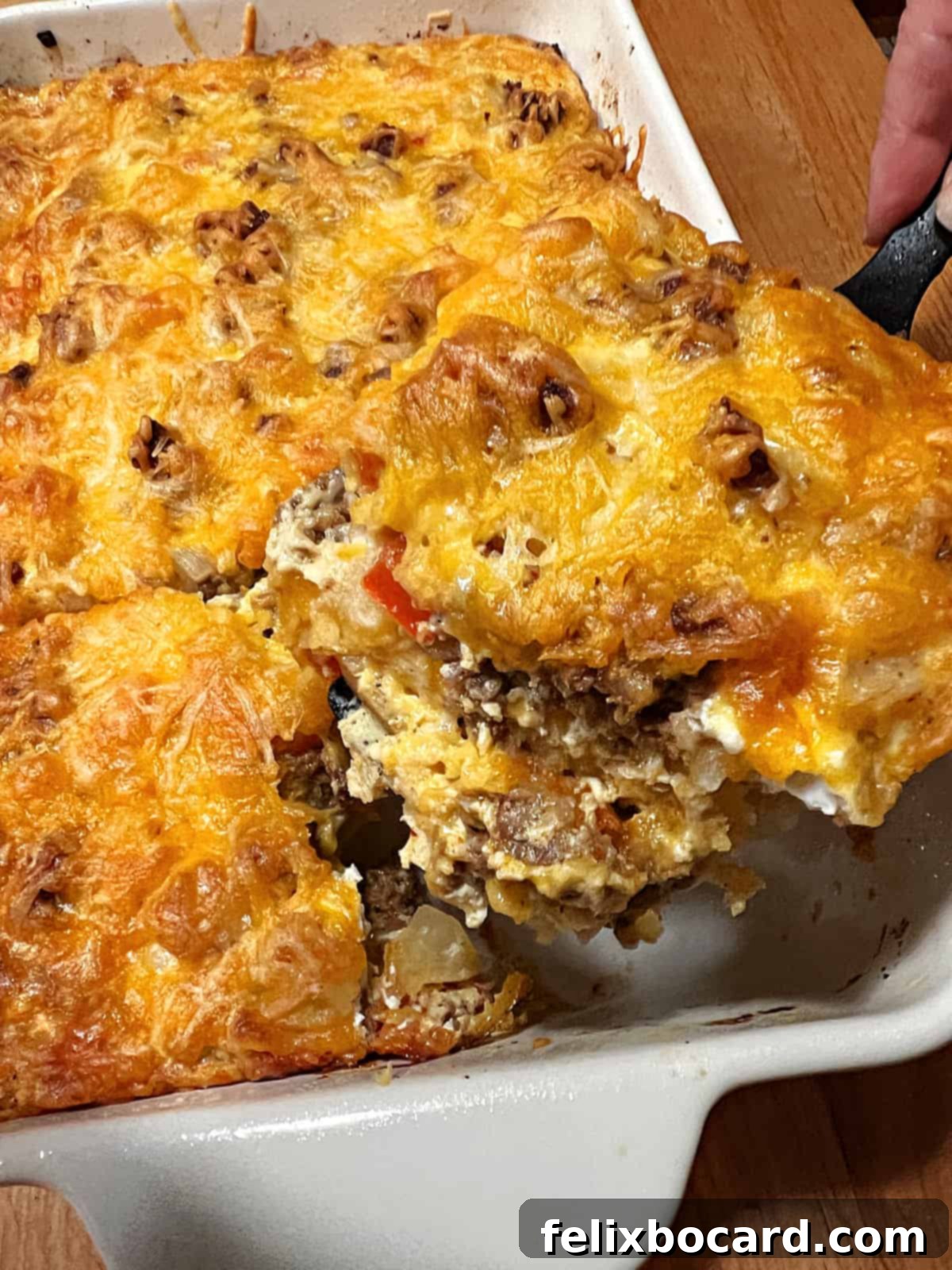 A spatula lifting a perfectly cut square serving of Chorizo Egg Bake from the baking pan, showing its golden-brown top and layered interior.