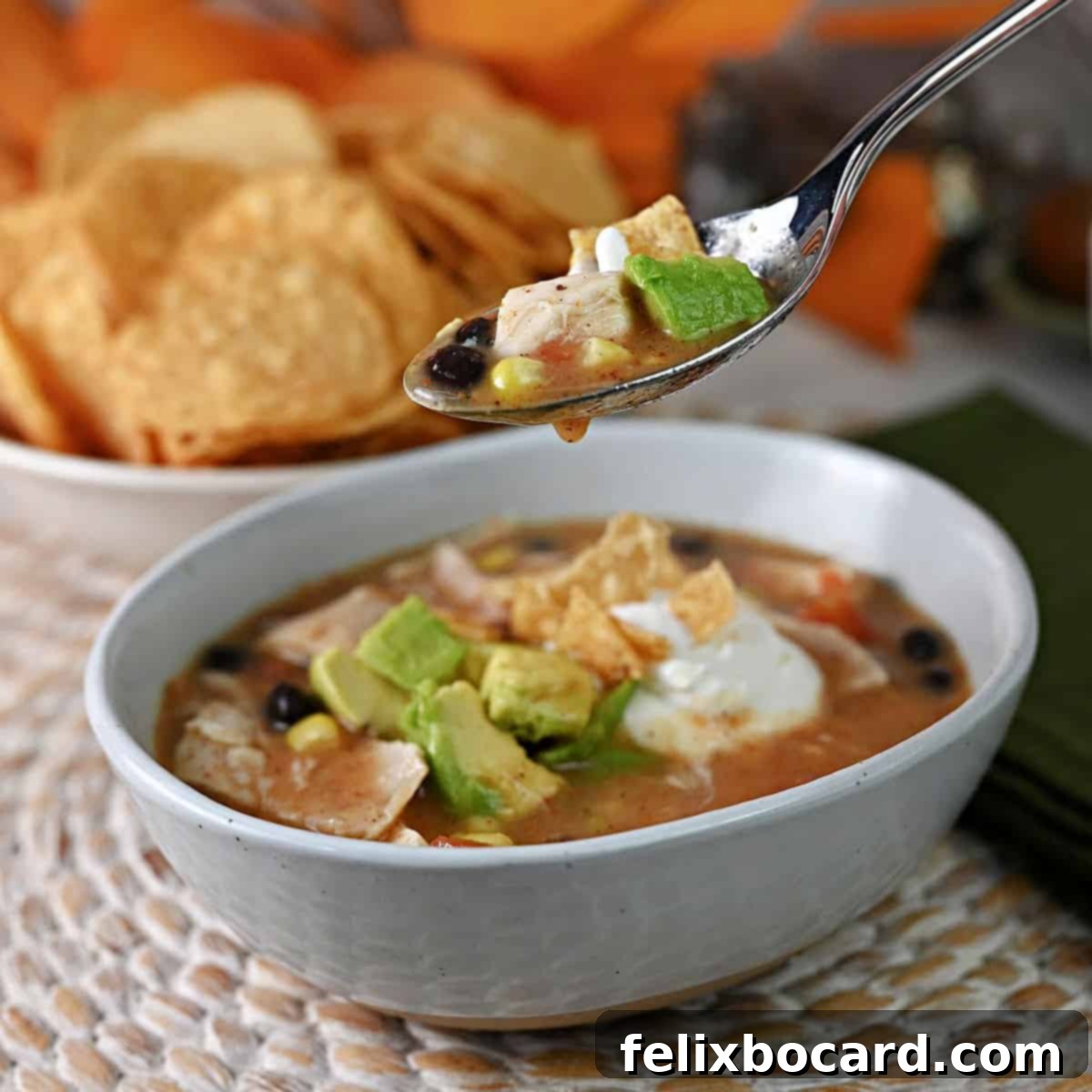 21 Delicious Makeovers for Your Leftover Shredded Chicken 15 A spoon full of vibrant chicken tortilla soup suspended over a brimming bowl, ready to be enjoyed.