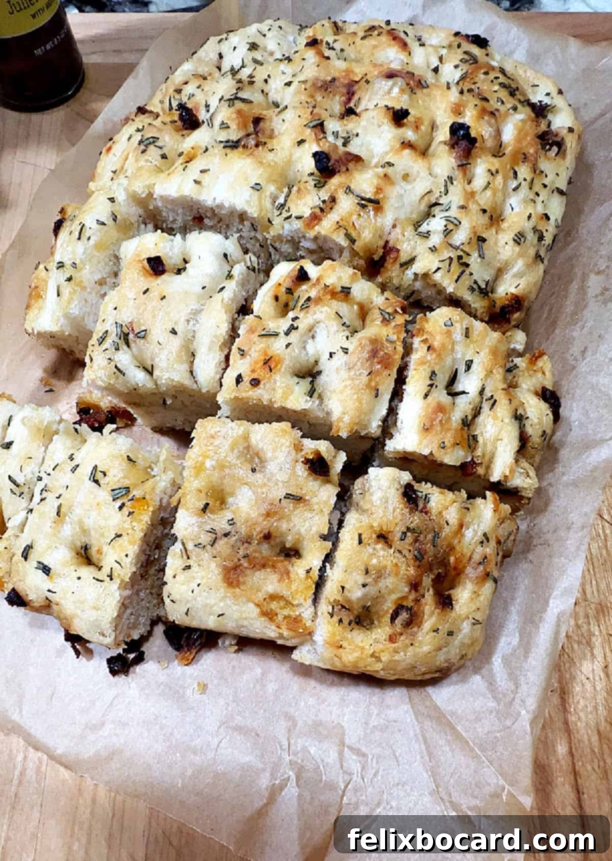 Simple Sun-Dried Tomato & Rosemary Focaccia 10 Freshly baked sun-dried tomato focaccia being cut into squares with a pizza cutter on a wooden board, ready for serving.