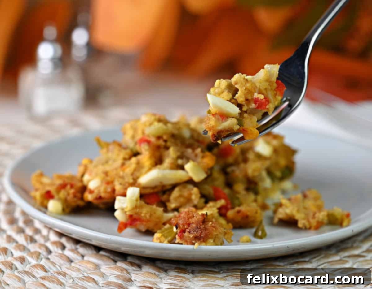 Close-up of a fork holding a spoonful of cornbread dressing, clearly showing the details including the finely chopped hard-boiled eggs amidst the golden cornbread.