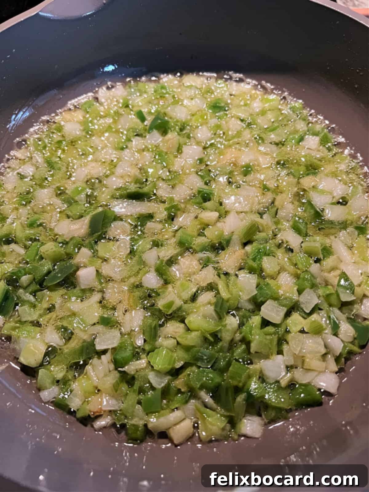Close-up of chopped vegetables (onions, celery, green bell pepper) gently cooking in melted butter in a large skillet, softening to release their aromas.