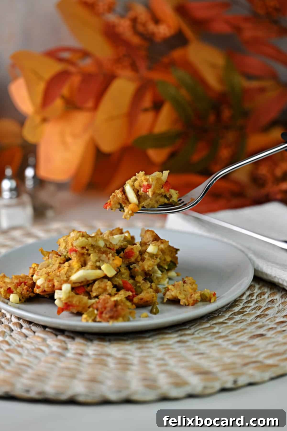 A fork lifts a generous bite of cornbread dressing, with a visible piece of hard-boiled egg, suspended over a serving plate of the dish.