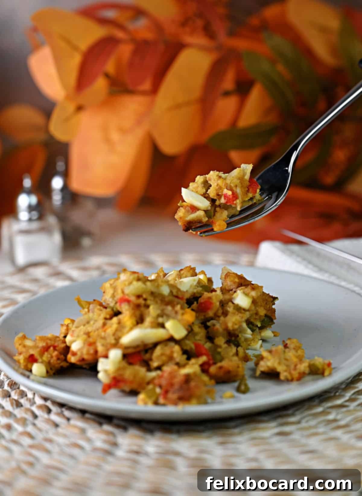 A fork holding a piece of cornbread dressing, clearly showcasing a visible piece of hard-boiled egg, ready to be eaten.