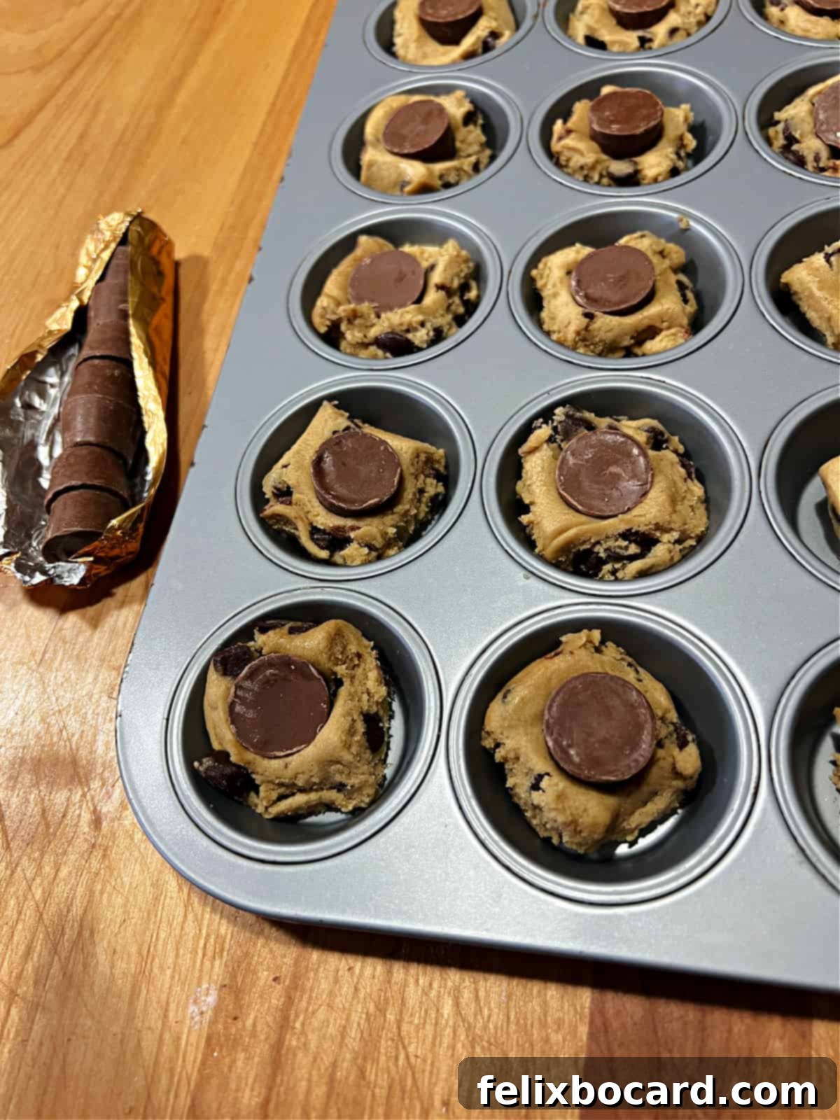 A single unwrapped Rolo candy being pressed into a square of cookie dough in a mini muffin pan.