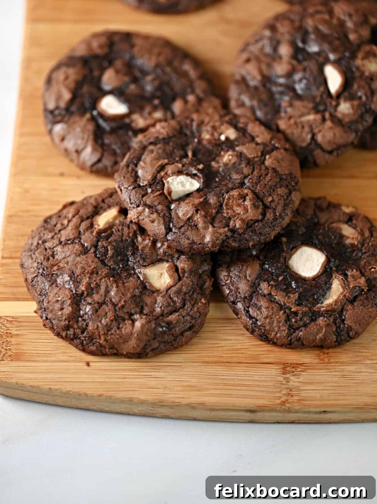 Chocolate malted milk ball cookies stacked on a cutting board.