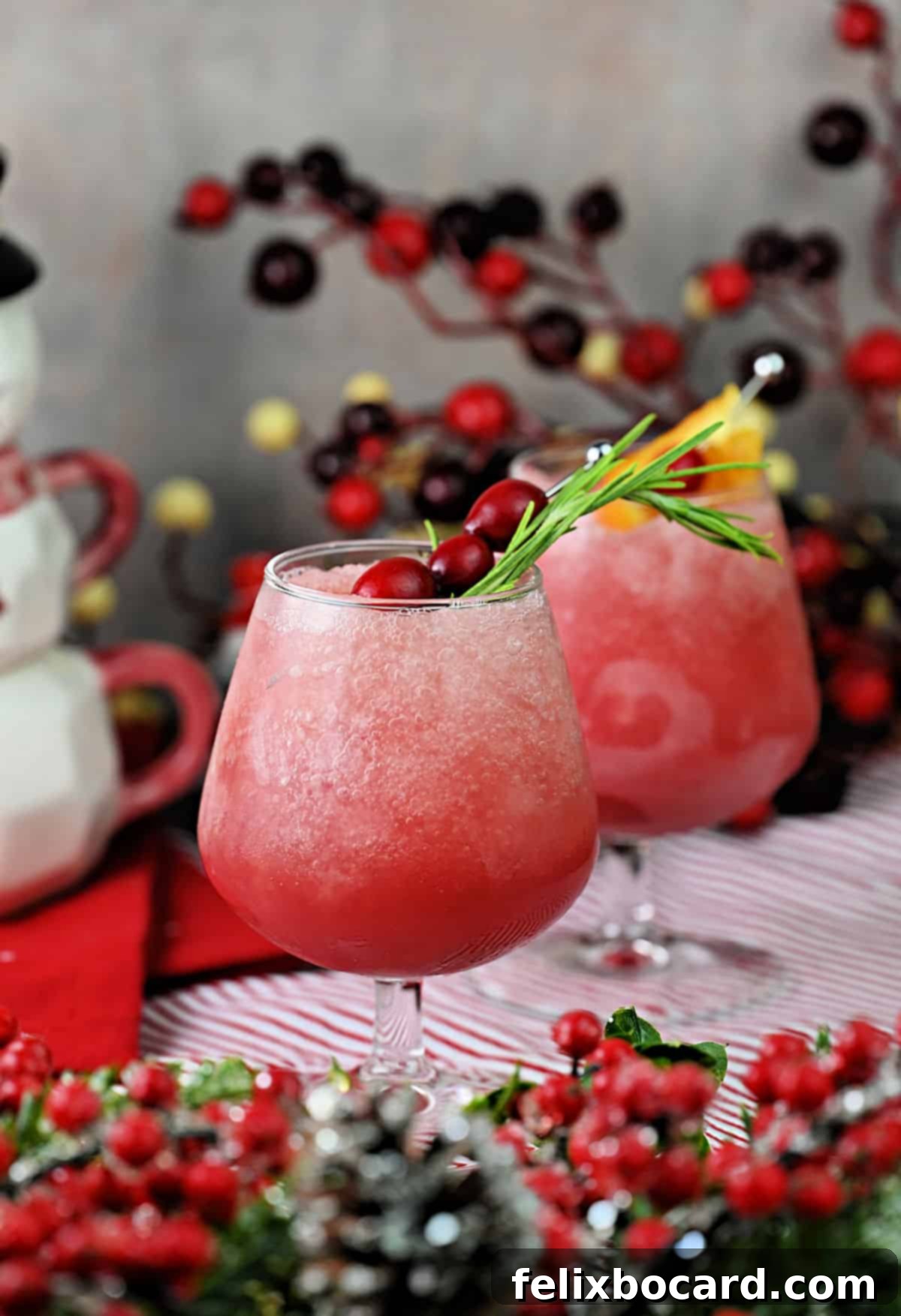 2 glasses of cranberry daiquiri rum slush garnished with cranberries, rosemary, and orange.