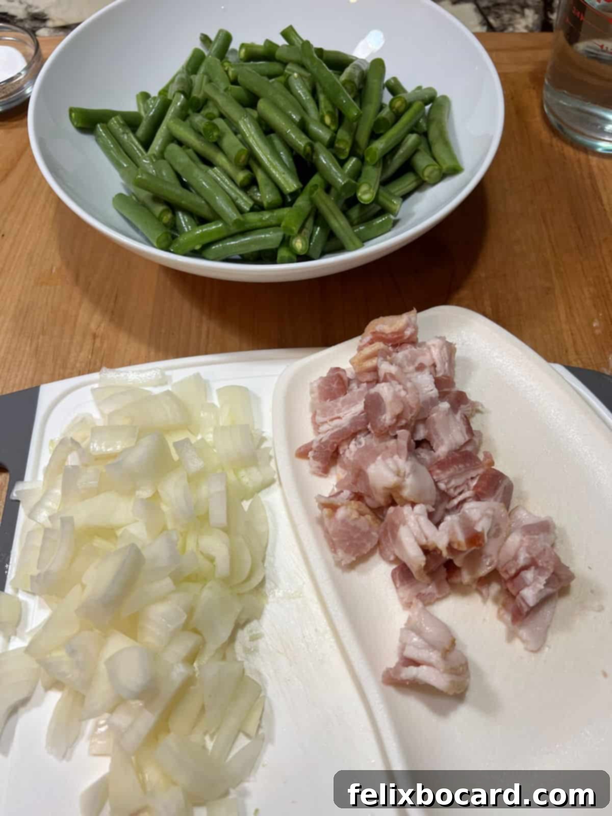 Prepared green beans, diced onion, and raw bacon in separate bowls, ready for cooking.