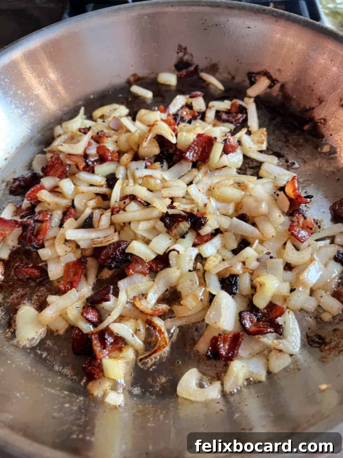 Cooked onion and crispy bacon simmering together in a cast-iron skillet, creating a flavorful base.