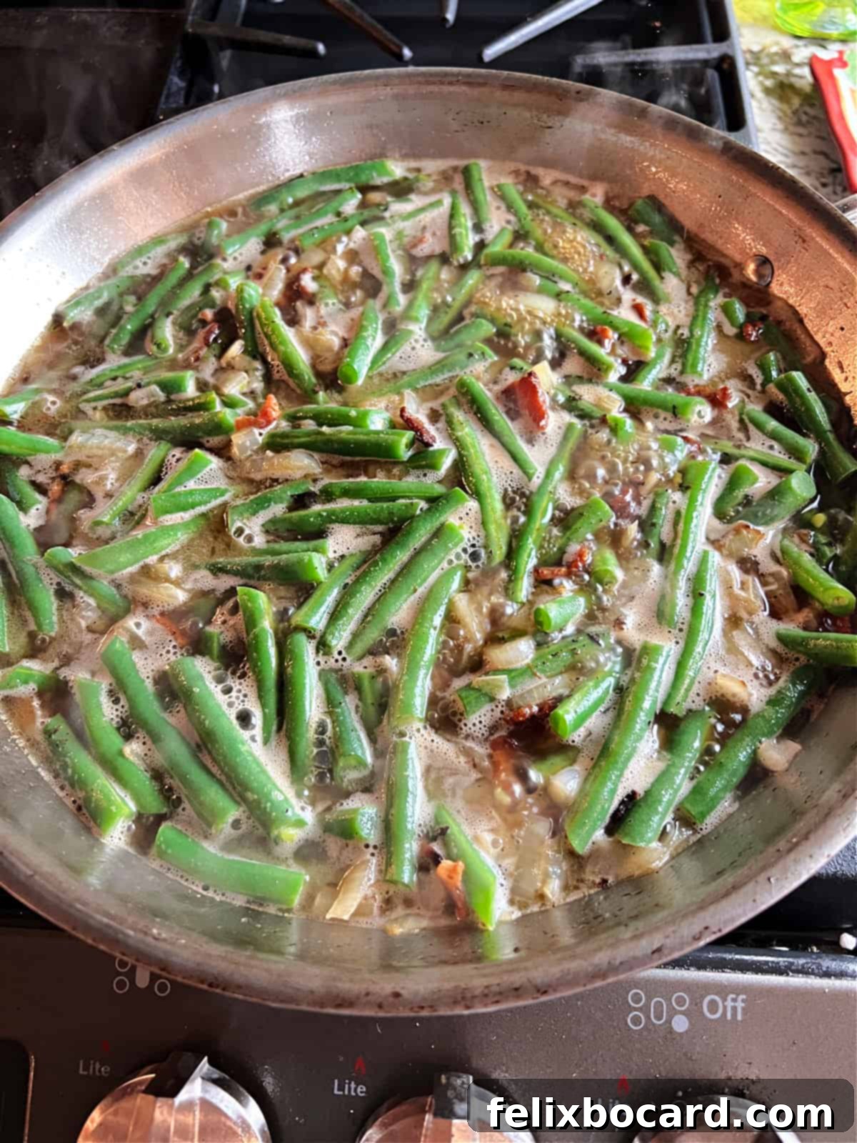 Green beans simmering in a skillet with the liquid, absorbing the rich flavors.